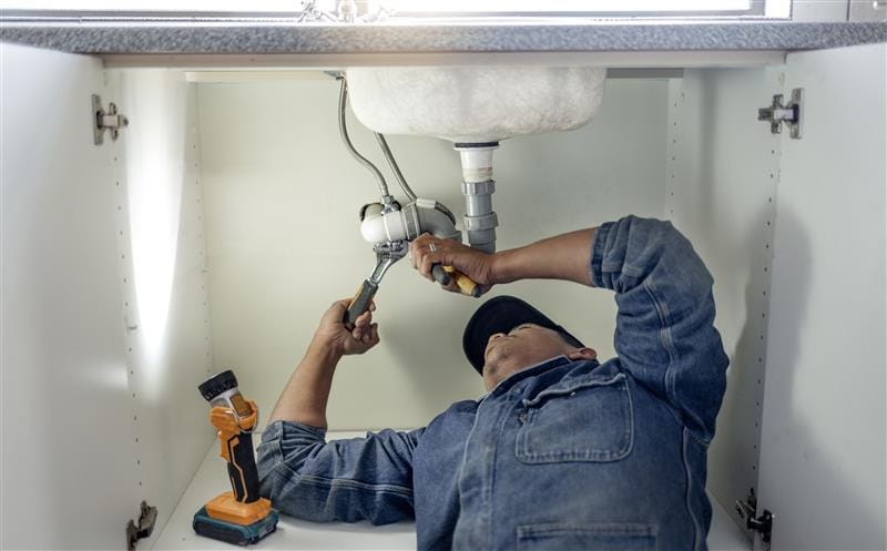 Plumber repairing pipes beneath a bathroom sink in New Smyrna Beach