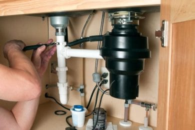 Plumber repairing a garbage disposal beneath a kitchen sink in New Smyrna Beach