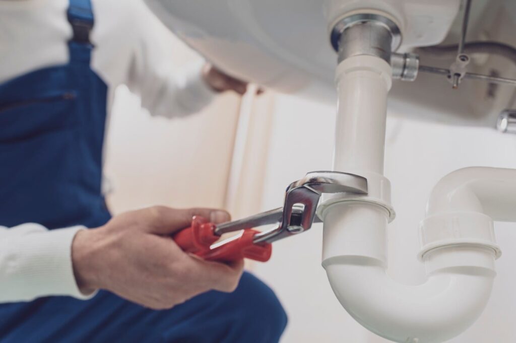 Plumber repairing a white drain pipe beneath a sink in New Smyrna Beach