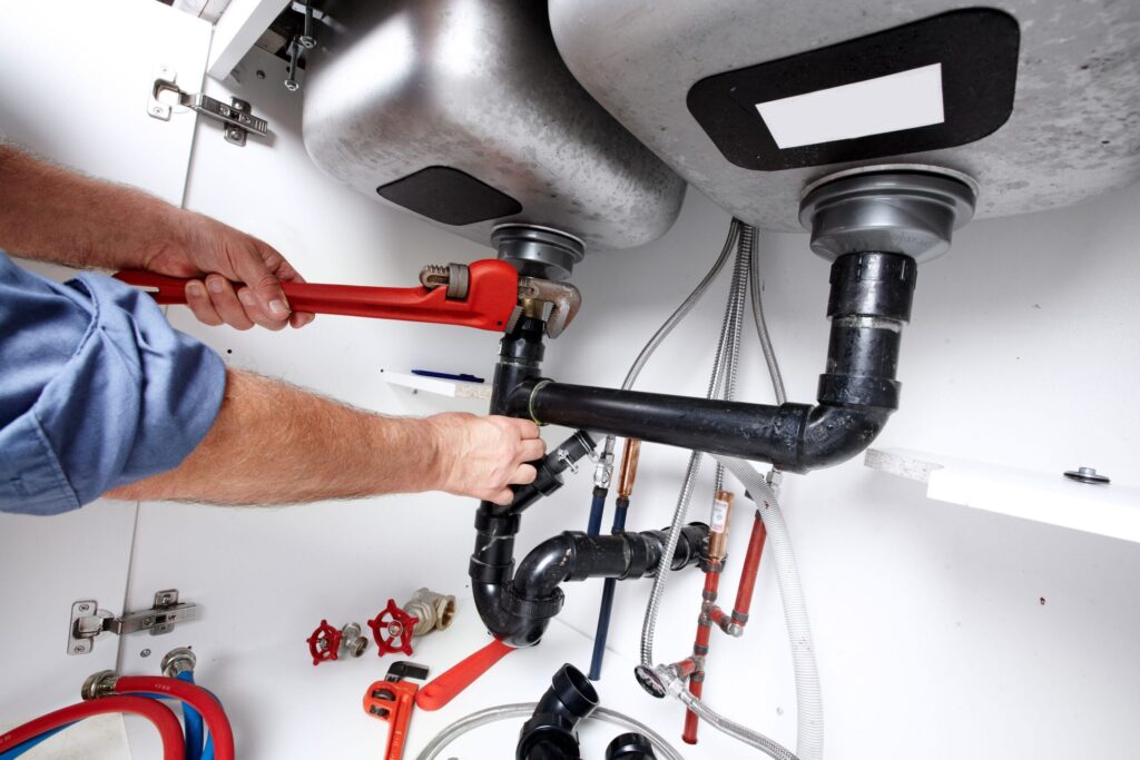 Plumber repairing drain pipes beneath a kitchen sink in New Smyrna Beach